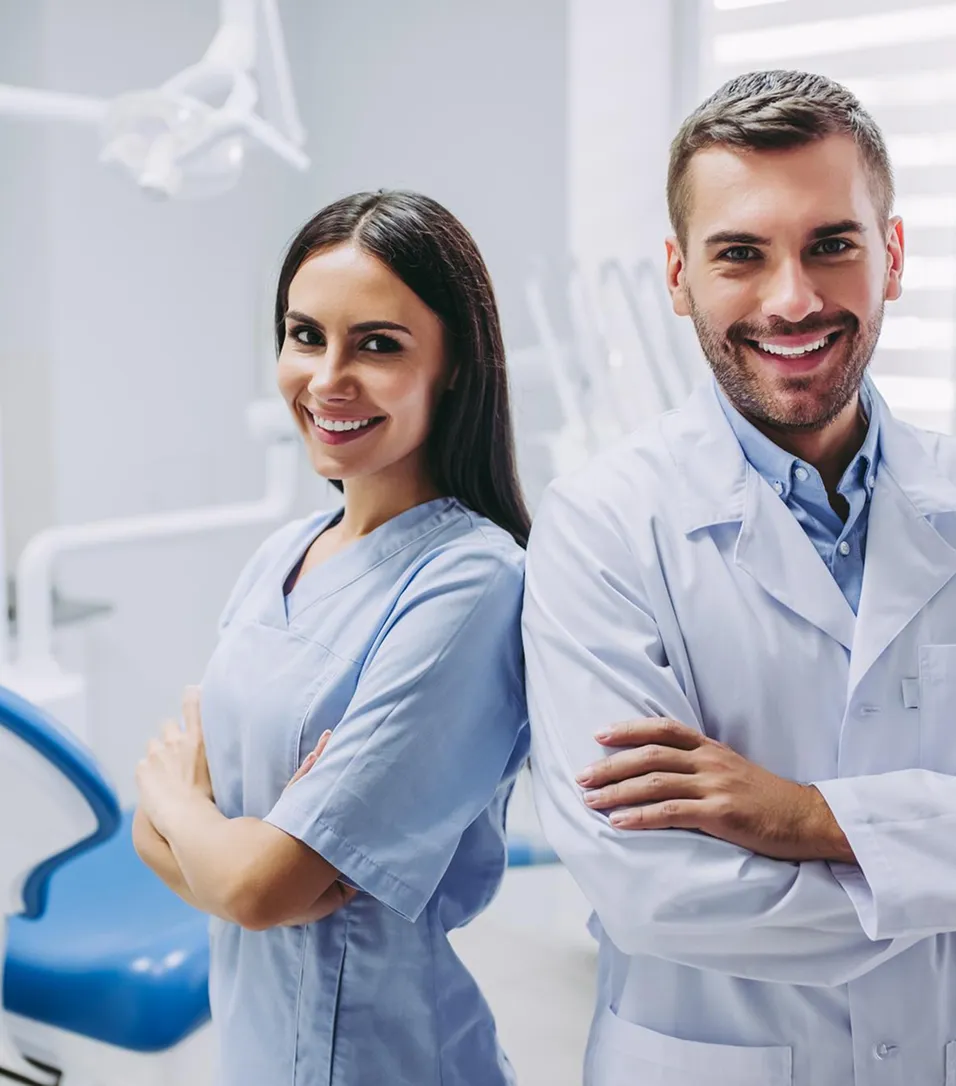 Two smiling members of the dental team stand side by side in a treatment room